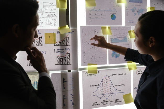 male female colleagues standing by window looking business graphs it 1098 20205